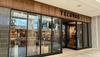 Exterior of a Tecovas store in a shopping mall, showing large glass windows and a wooden sign above the entrance.