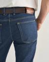A person wearing blue jeans with yellow stitching, a brown leather belt, and a white shirt, shown from the back waist down.