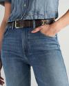 Person wearing a blue denim jacket and jeans with a brown leather belt, standing with one hand in their pocket.