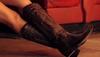 A person wearing dark brown cowboy boots with decorative stitching, resting their legs on a red seat.