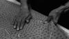 A person’s hands work with a textured, spotted fabric on a flat surface; one hand stretches the material while the other holds it steady.