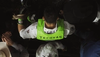 A person with "Tecovas" on their green vest is seen from behind, surrounded by others, some holding ropes.